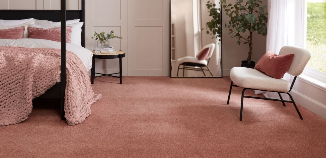 A rose coloured sparkle carpet laid in a bedroom with four poster bed, mirror and chair.