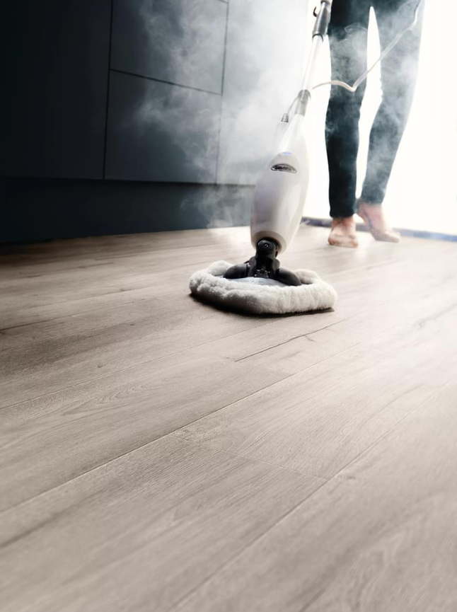 Light laminate flooring with a steam mop and dark kitchen units in the background