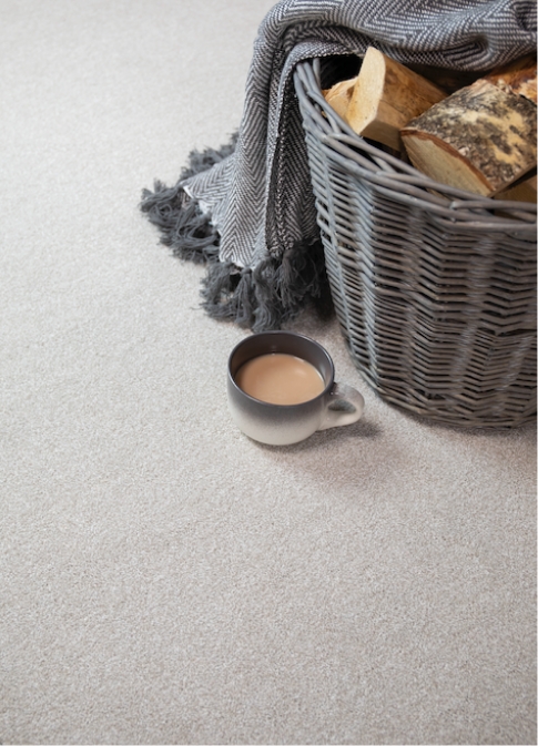 A close up shot of a wicker log basket and cup of tea on a grey carpet.