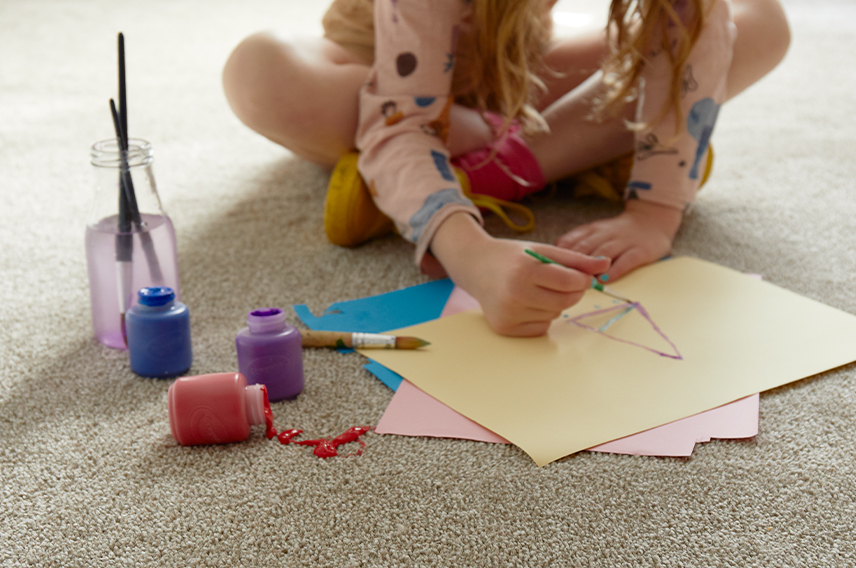 A girl is sitting on the floor painting, whilst a red paint pot has been knocked over